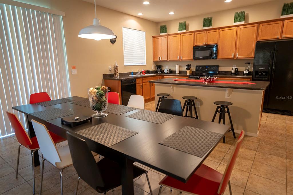 A kitchen and dining area with wooden cabinets, a black refrigerator, and a long table — 1039 TOURMALINE DRIVE, KISSIMMEE, FL