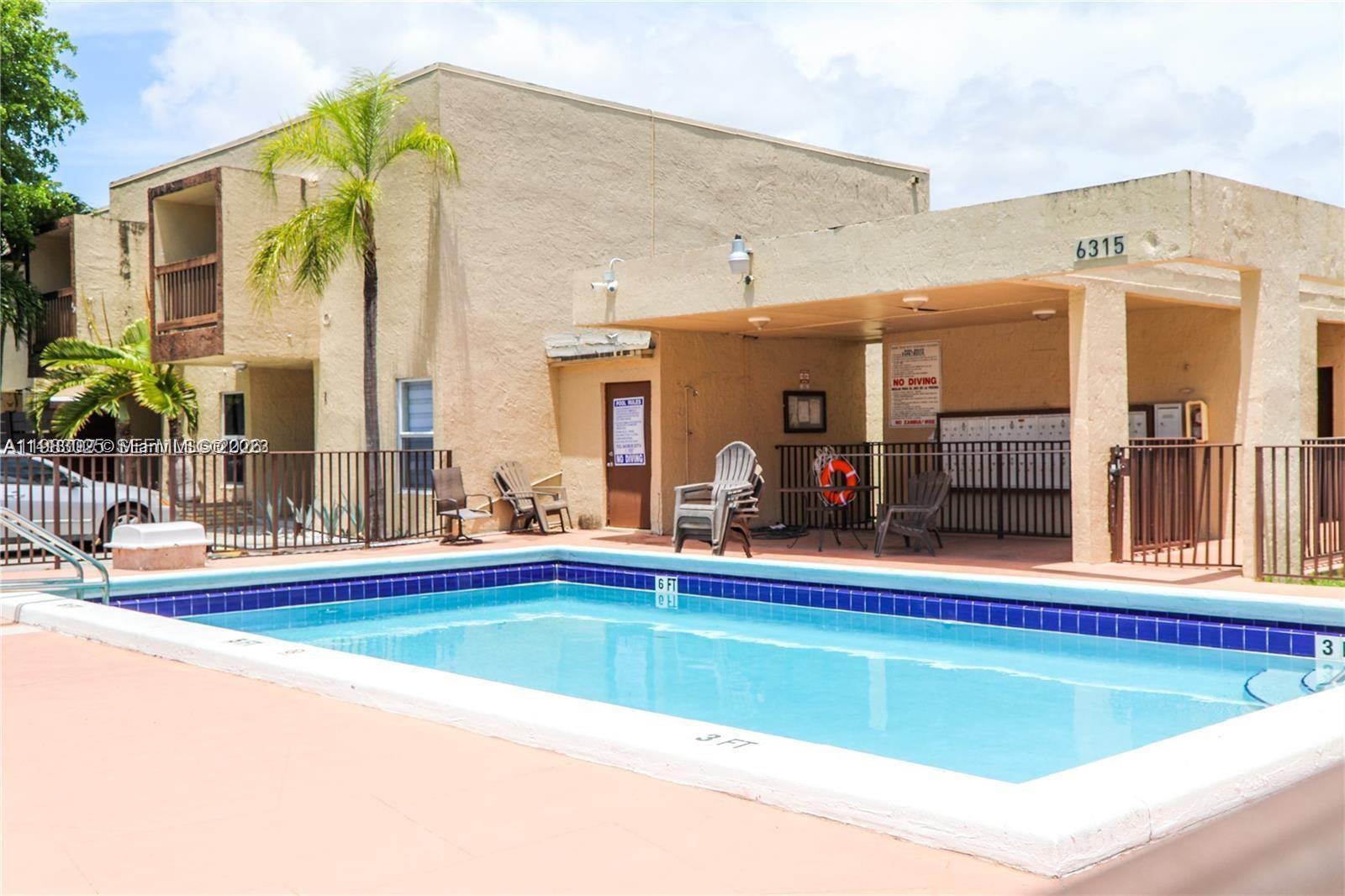 A rectangular swimming pool sits in front of a tan building with a covered patio — 6335 SW 138th Ct # 1, Miami FL 33183, MIAMI, FL
