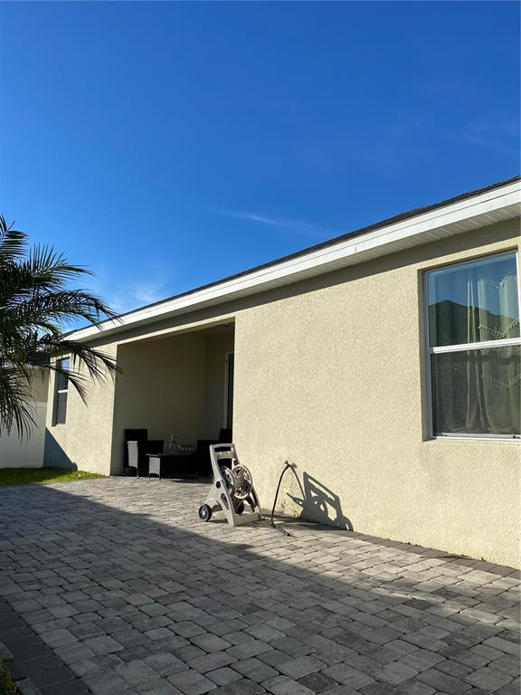 A paved patio area sits outside a stucco house with a covered porch and window — 3016 MADELIA LANE, KISSIMMEE, FL