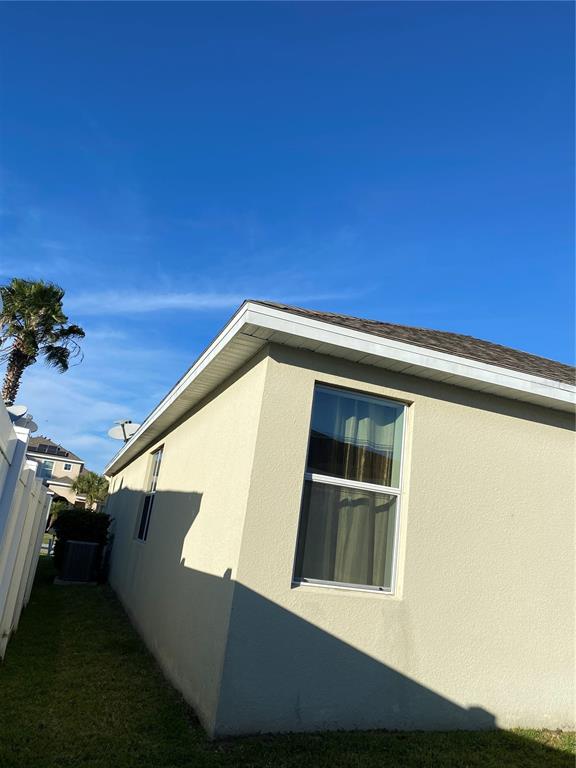 The exterior side view of a house features beige stucco walls and a single window — 3016 MADELIA LANE, KISSIMMEE, FL