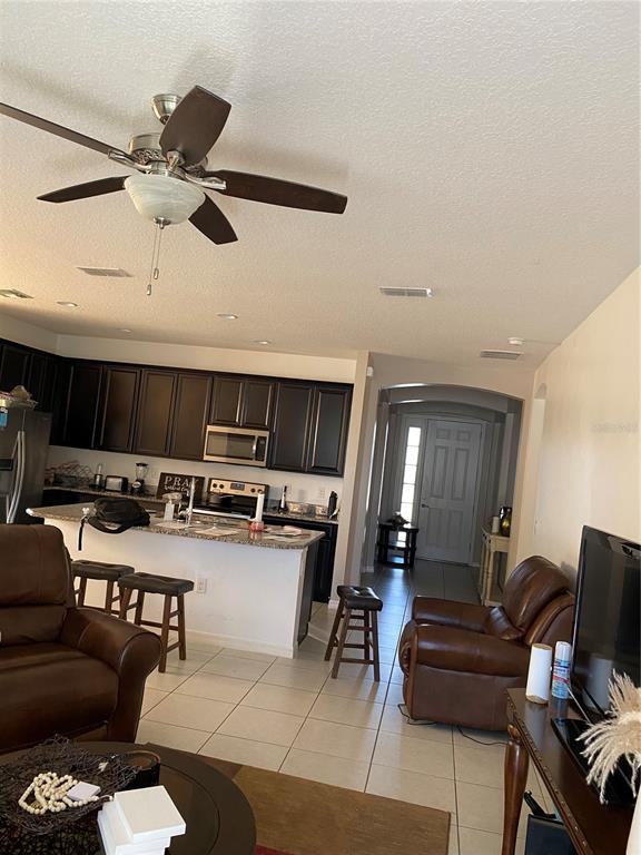 A kitchen with dark cabinets and a breakfast bar overlooks a living area — 3016 MADELIA LANE, KISSIMMEE, FL