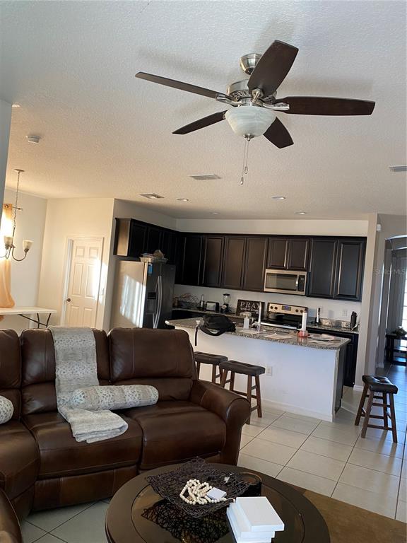 A living room with a brown leather sofa faces an open kitchen with dark cabinets — 3016 MADELIA LANE, KISSIMMEE, FL