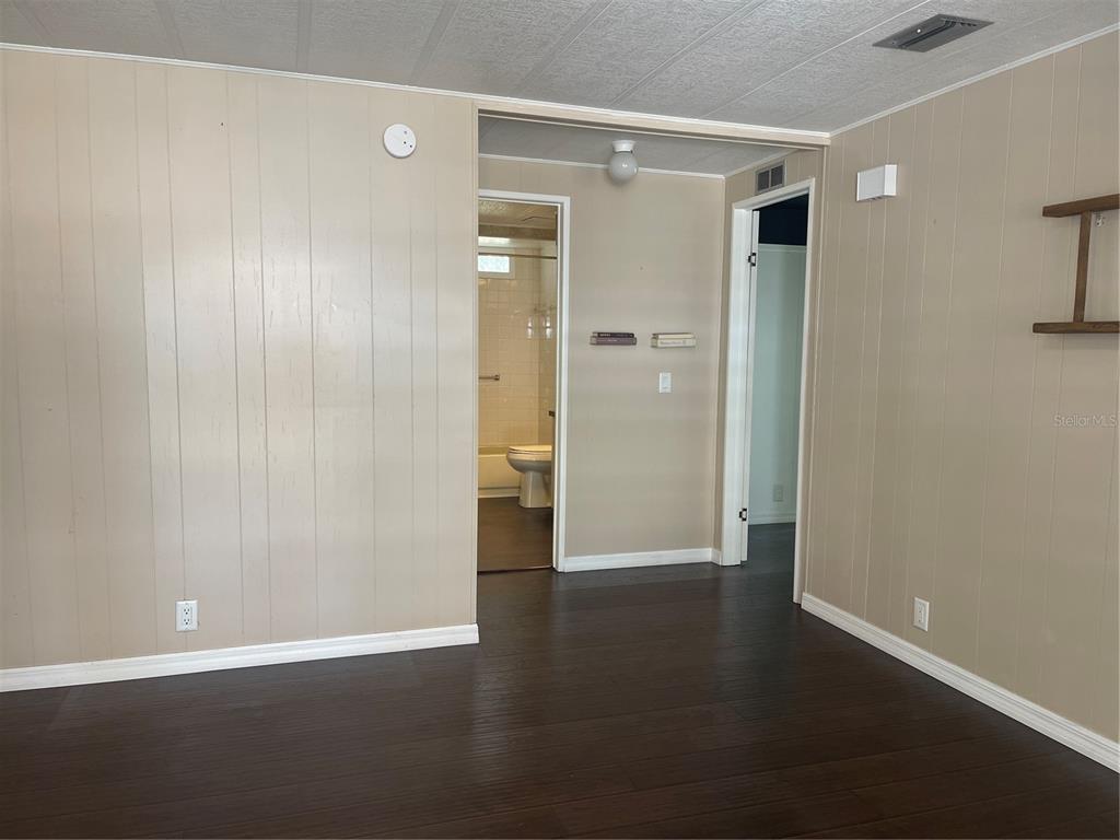 An interior view shows a room with wood-look flooring, beige paneling, and two doorways — 52 N BOBWHITE RD, WILDWOOD, FL