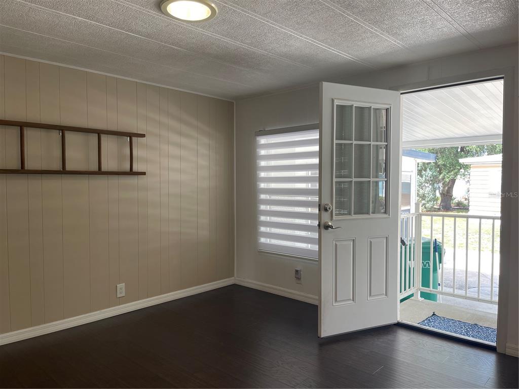 A room with wood-look flooring, paneled walls, a ladder shelf, and an open exterior door — 52 N BOBWHITE RD, WILDWOOD, FL