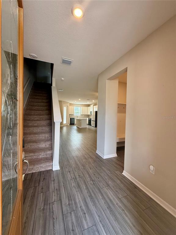 An entryway with wood-look tile flooring leads to a staircase and an open-concept kitchen — 11357 CAY SPRUCE WAY, SAN ANTONIO, FL