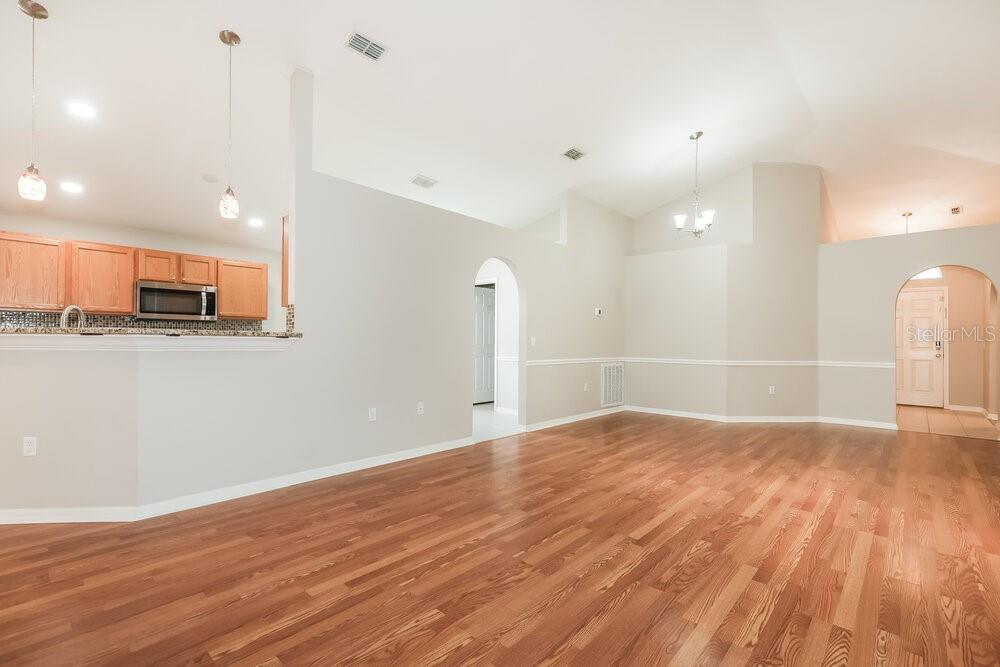 An open-concept living area features hardwood floors, vaulted ceilings, and an adjacent kitchen with cabinets — 1309 ALHAMBRA CREST DRIVE, RUSKIN, FL