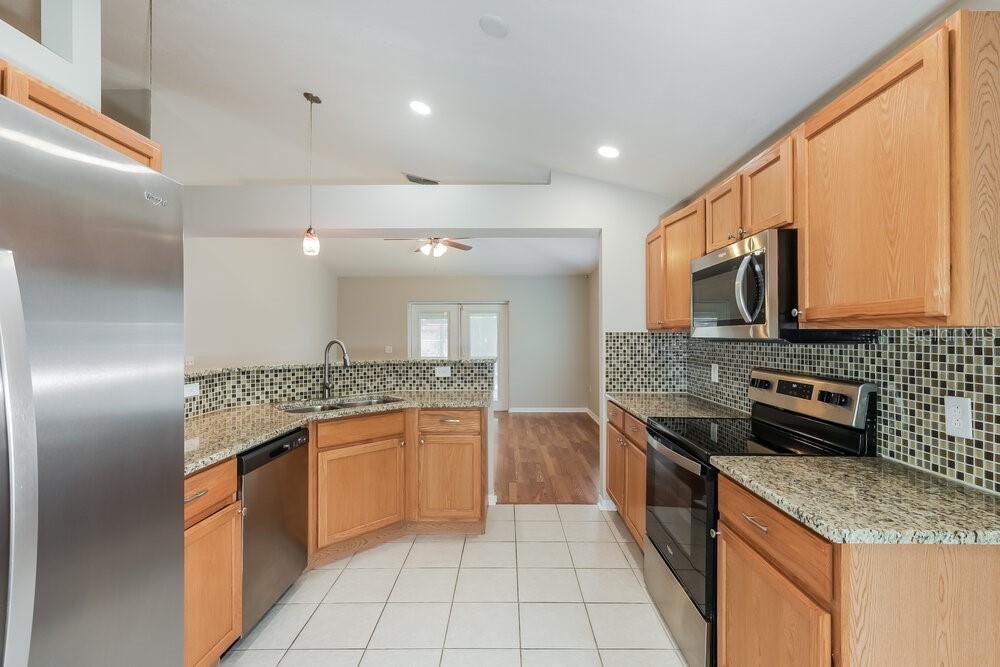 A kitchen with light wood cabinets, granite countertops, tile backsplash, and stainless steel appliances — 1309 ALHAMBRA CREST DRIVE, RUSKIN, FL