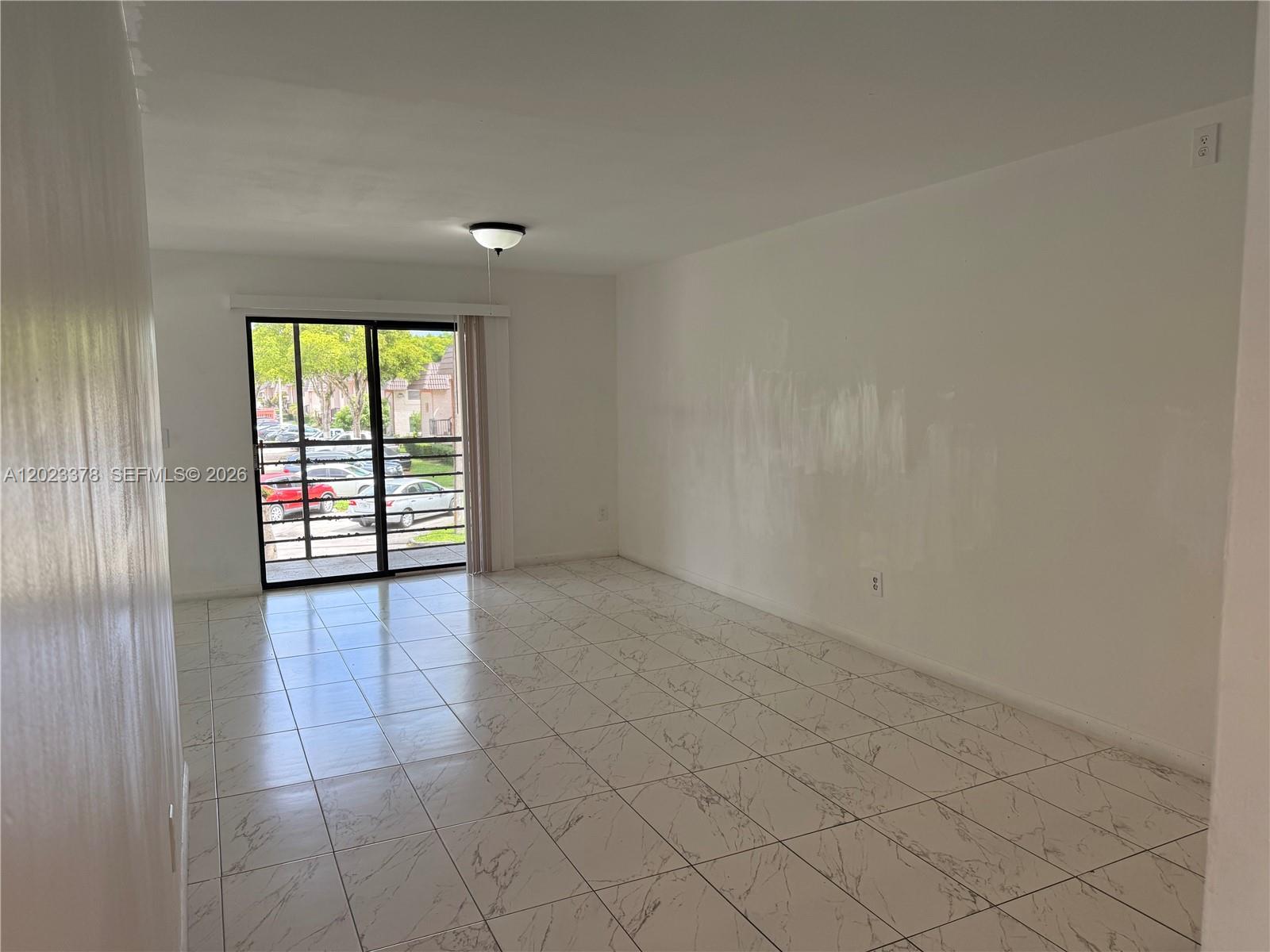 An empty living room features white marble-look tile flooring and a sliding glass door — 20825 NE 8th Ct # 19, Miami FL 33179, MIAMI, FL