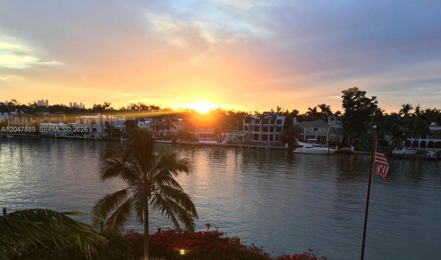 A sunset view over a canal with waterfront houses, palm trees, and a boat — 5700 Collins Ave # 6J, Miami Beach FL 33140, MIAMI BEACH, FL