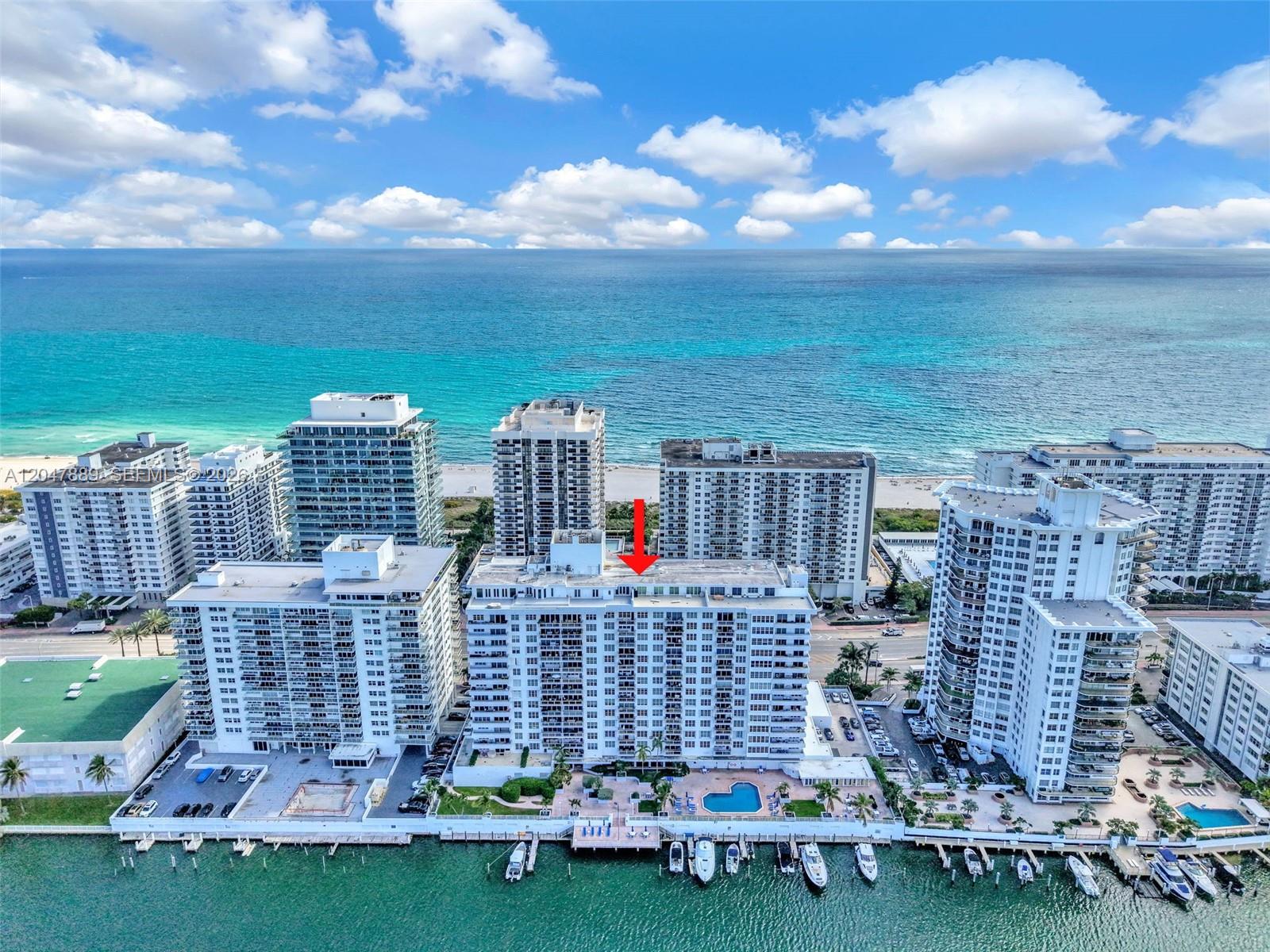 An aerial view shows a white high-rise condominium building with a pool and boat docks — 5700 Collins Ave # 6J, Miami Beach FL 33140, MIAMI BEACH, FL
