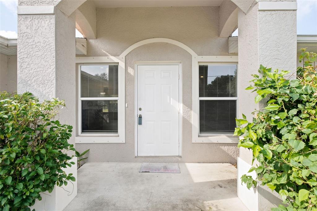 A white front door is centered between two windows on a covered concrete porch — 4171 MAGENTA AVENUE, NORTH PORT, FL