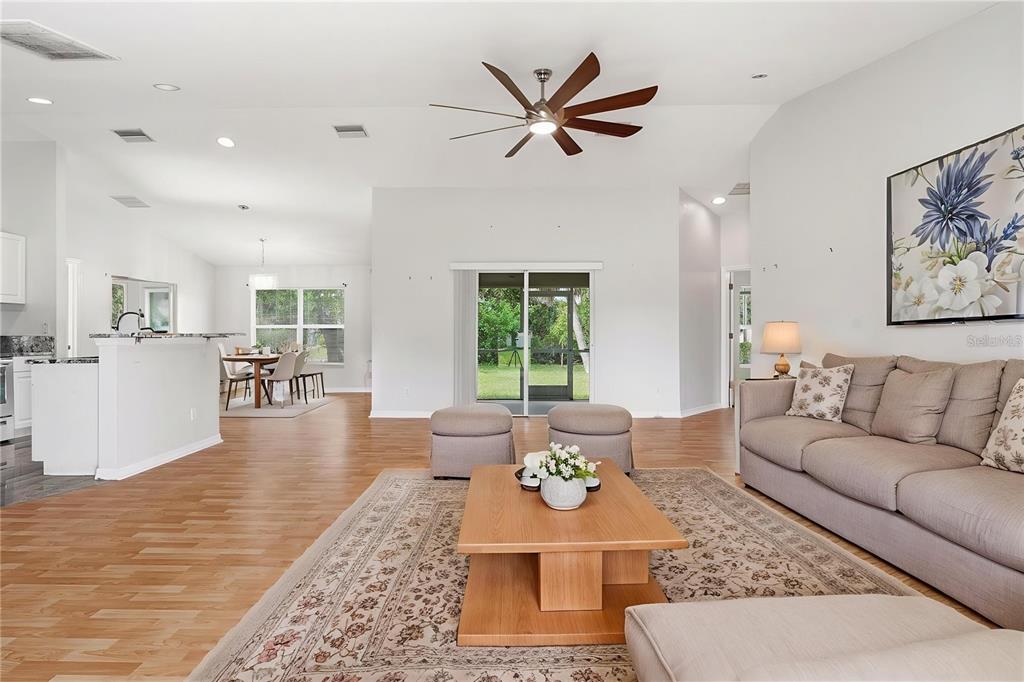 A spacious living room features light wood flooring, a ceiling fan, and a neutral sofa — 4171 MAGENTA AVENUE, NORTH PORT, FL