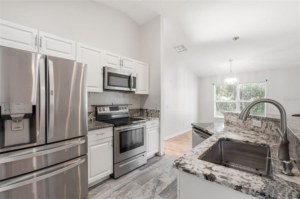 A kitchen features white cabinets, granite countertops, stainless steel appliances, and gray tile flooring — 4171 MAGENTA AVENUE, NORTH PORT, FL