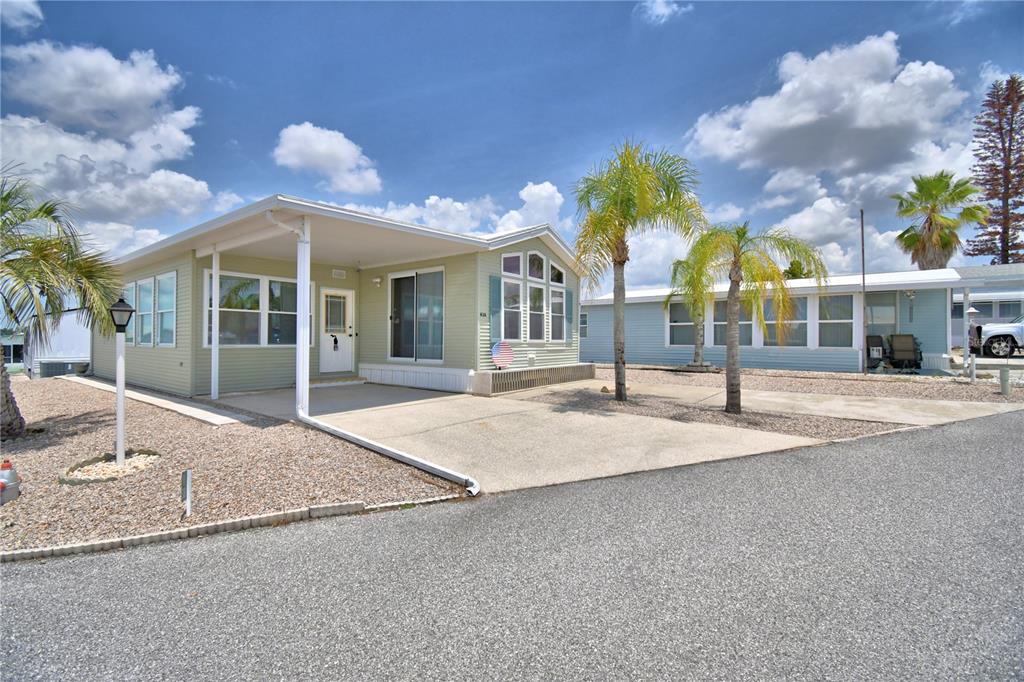 A light green manufactured home with a carport and palm trees under a cloudy sky — 251 PATTERSON ROAD UNIT H38, HAINES CITY, FL