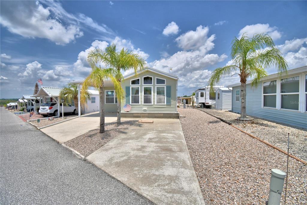 A light green manufactured home with a concrete driveway and palm trees in a park — 251 PATTERSON ROAD UNIT H38, HAINES CITY, FL