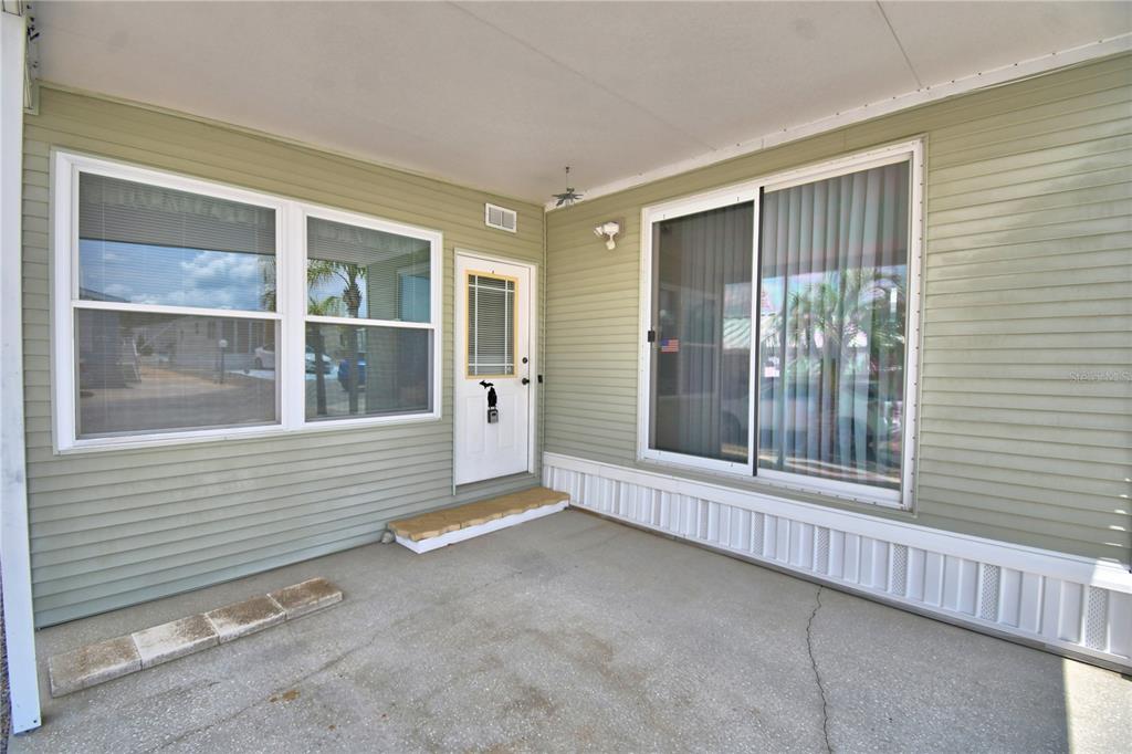 A covered concrete patio features light green horizontal siding, a white door, and sliding glass doors — 251 PATTERSON ROAD UNIT H38, HAINES CITY, FL