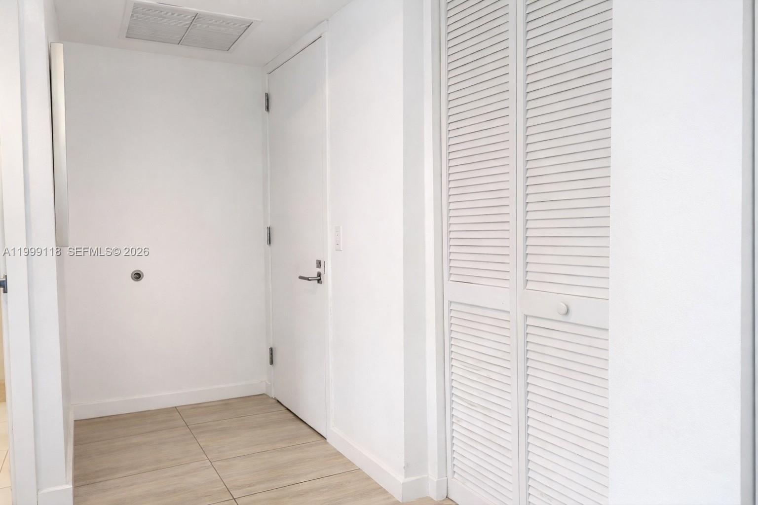 A hallway features white walls, light-colored tile flooring, a closed door, and a louvered closet — 31 SE 6th St # 301, Miami FL 33131, MIAMI, FL