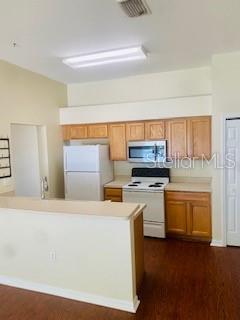 A kitchen features light wood cabinets, white appliances, and a breakfast bar with wood flooring — 7731 MERCHANTVILLE CIRCLE, ZEPHYRHILLS, FL
