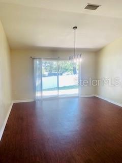 An empty room with dark wood-look flooring, a chandelier, and sliding glass doors to outside — 7731 MERCHANTVILLE CIRCLE, ZEPHYRHILLS, FL