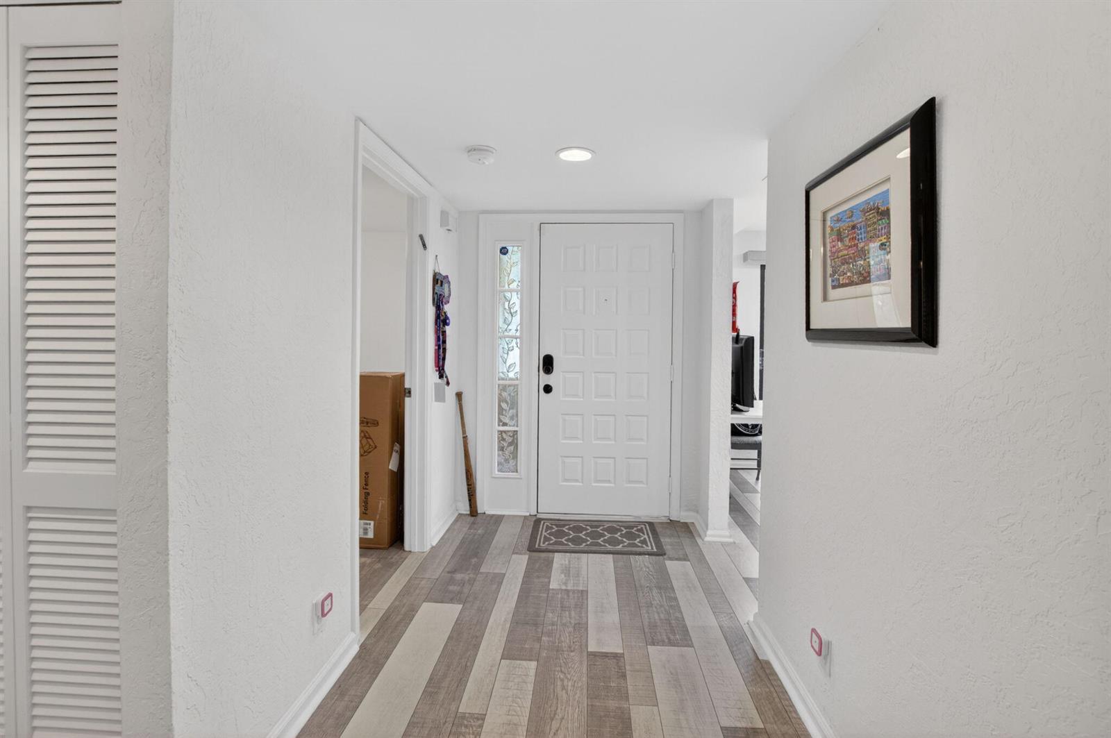 A bright entryway features white walls, wood-look plank flooring, and a white front door — 7254 Clunie Place # 15002, Delray Beach FL 33446, DELRAY BEACH, FL