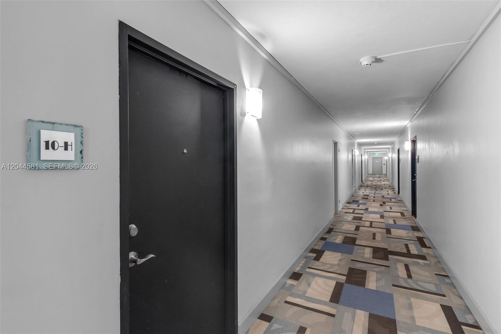 A long apartment hallway features a black door labeled 10-H and patterned carpet flooring — 7441 Wayne Ave # 10H, Miami Beach FL 33141, MIAMI BEACH, FL
