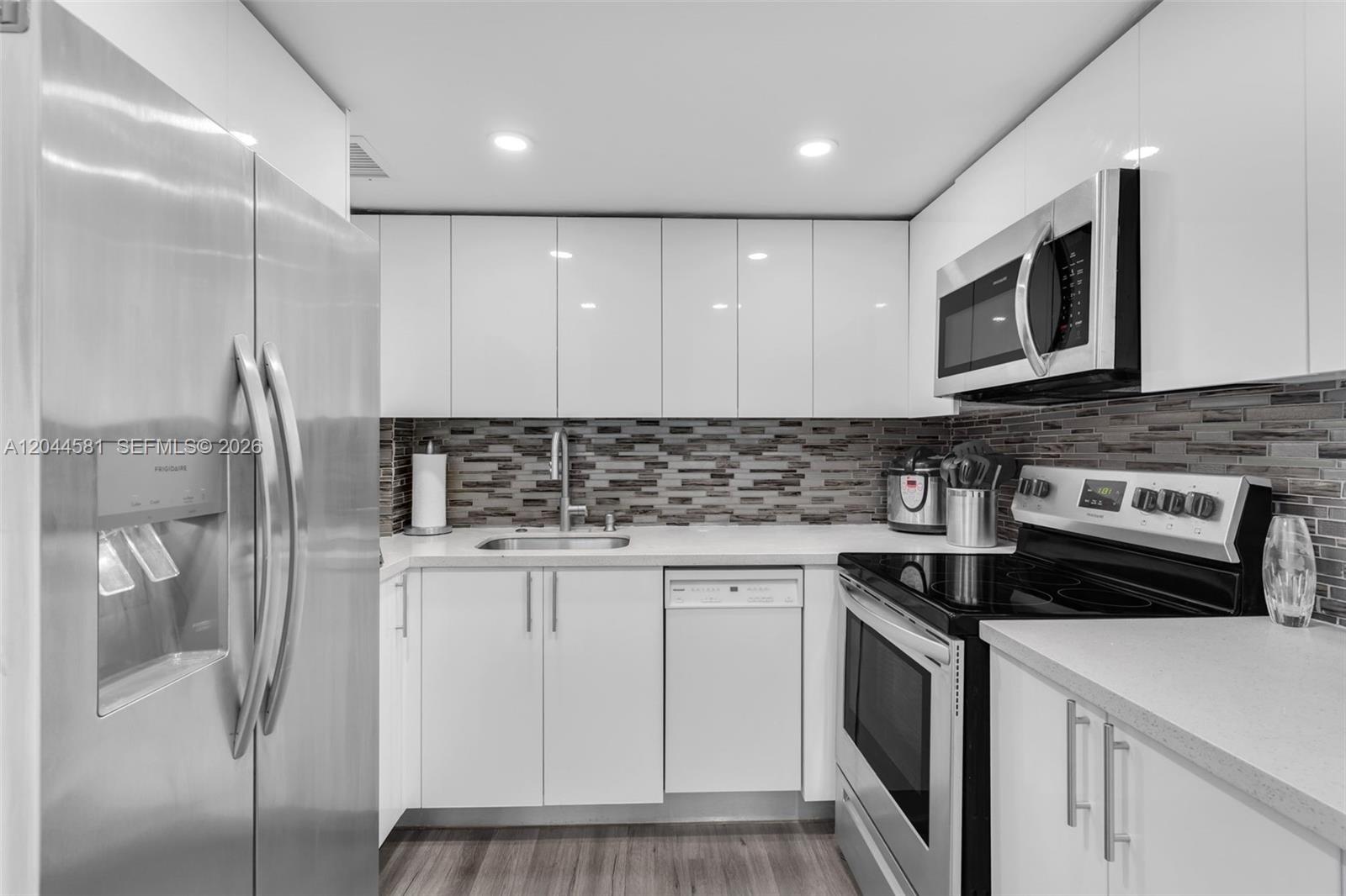 A kitchen features white flat-panel cabinets, stainless steel appliances, and a horizontal mosaic tile backsplash — 7441 Wayne Ave # 10H, Miami Beach FL 33141, MIAMI BEACH, FL