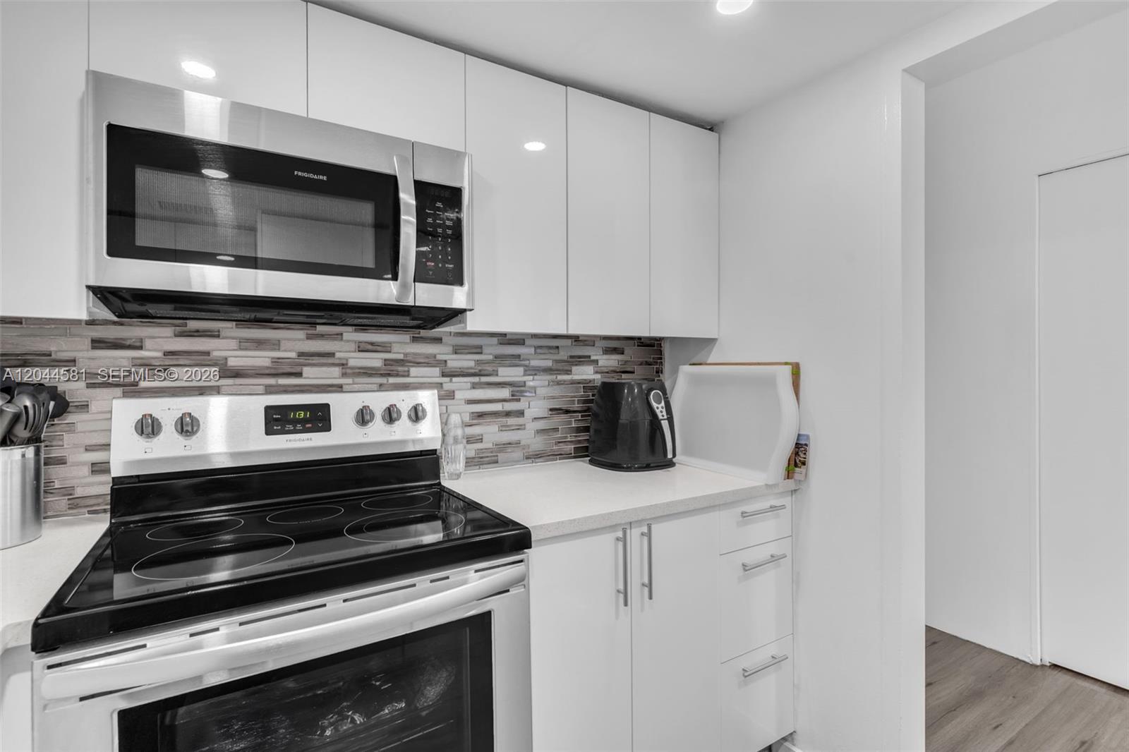 A kitchen features white cabinets, stainless steel appliances, and a horizontal tile backsplash — 7441 Wayne Ave # 10H, Miami Beach FL 33141, MIAMI BEACH, FL