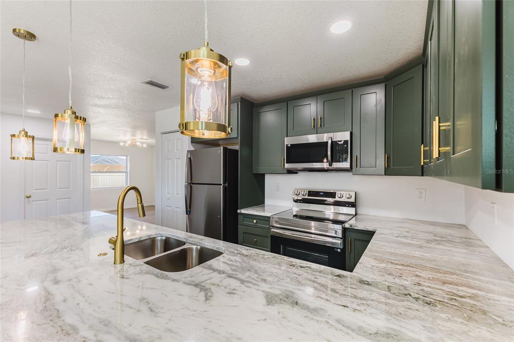 A kitchen features green cabinets, a marble countertop, stainless steel appliances, and gold pendant lights — 6254 SPINNAKER BOULEVARD, ENGLEWOOD, FL