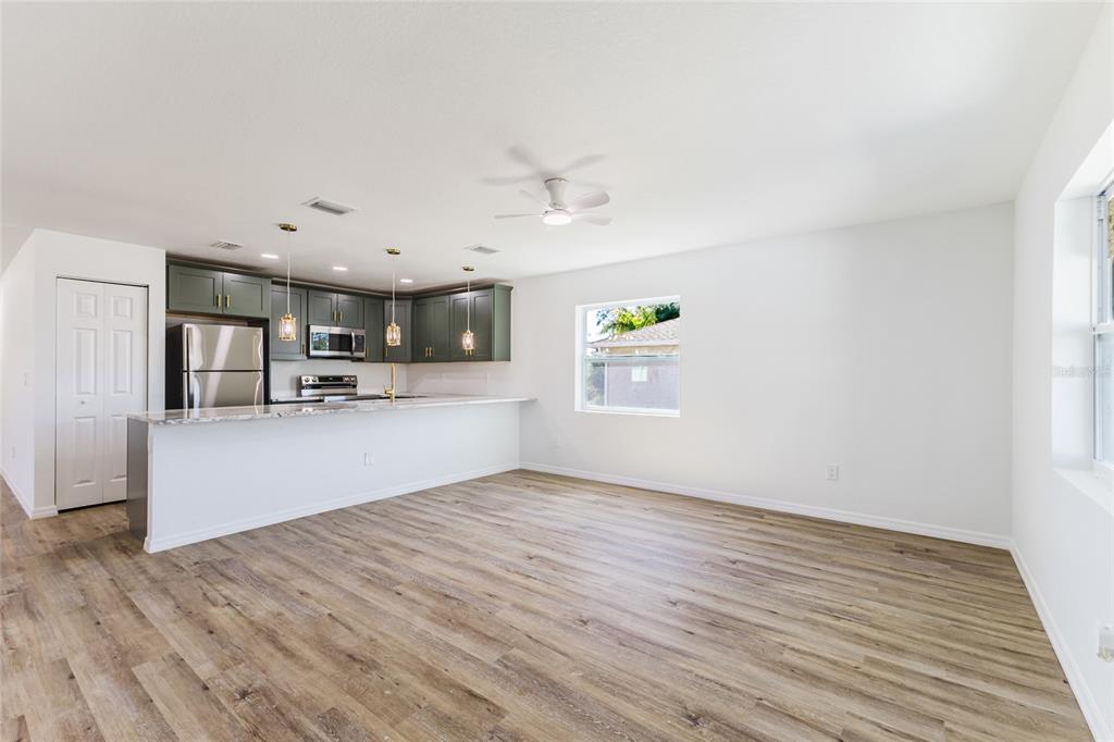 An open-concept kitchen with green cabinets and a breakfast bar overlooks a living area — 6254 SPINNAKER BOULEVARD, ENGLEWOOD, FL