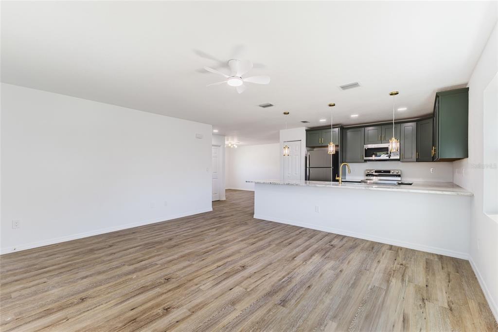 An open-concept kitchen with dark green cabinets and a breakfast bar overlooks a living area — 6254 SPINNAKER BOULEVARD, ENGLEWOOD, FL