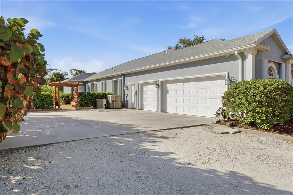 A gray house with a three-car garage and a wooden pergola in the yard — 750 HARMONY LANE, ENGLEWOOD, FL