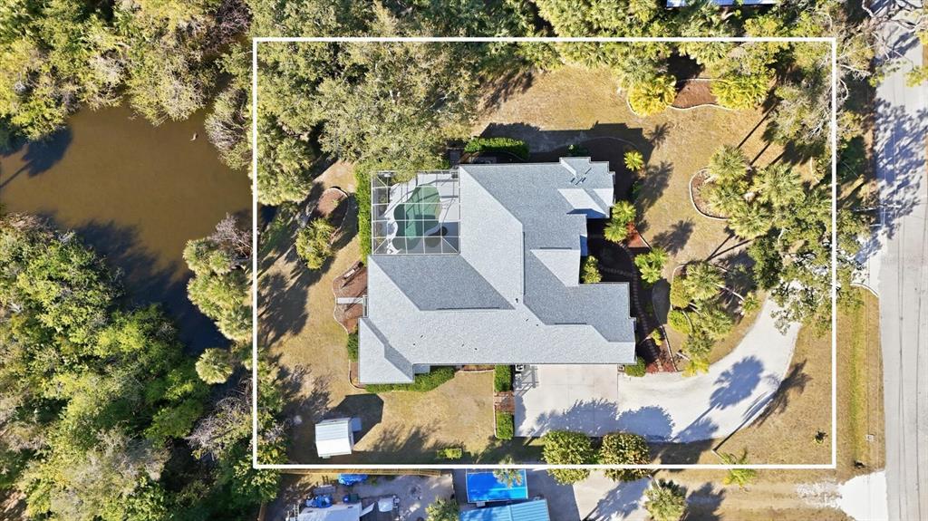 Aerial view of a house with a screened-in pool, driveway, and surrounding trees and pond — 750 HARMONY LANE, ENGLEWOOD, FL