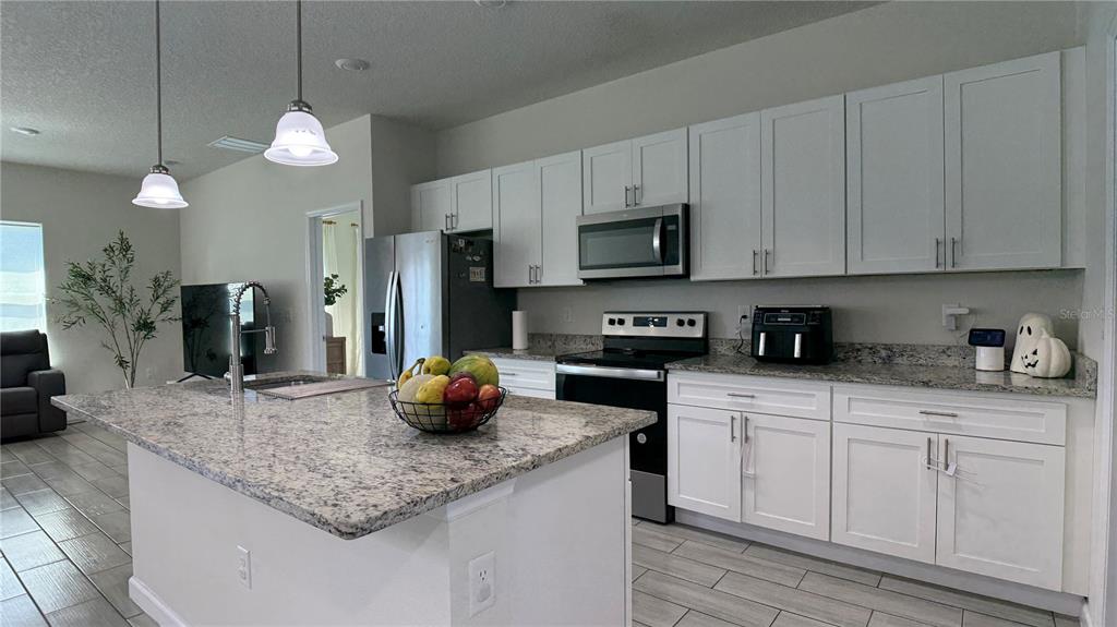 A kitchen with white cabinets, granite countertops, a center island, and stainless steel appliances — 2129 HIBISCUS PLACE, POINCIANA, FL