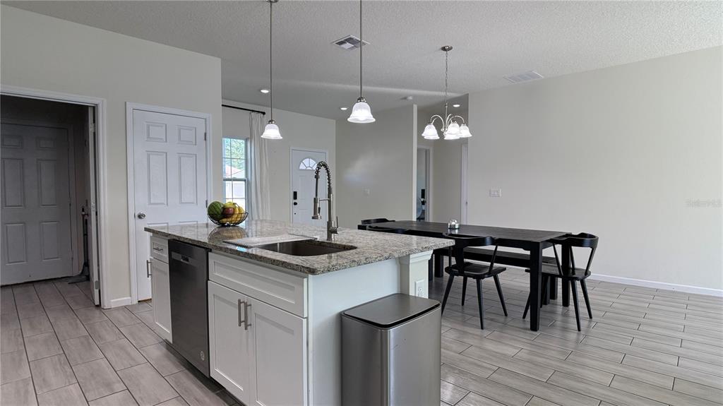 A kitchen island with a granite countertop and sink sits before a dining area — 2129 HIBISCUS PLACE, POINCIANA, FL