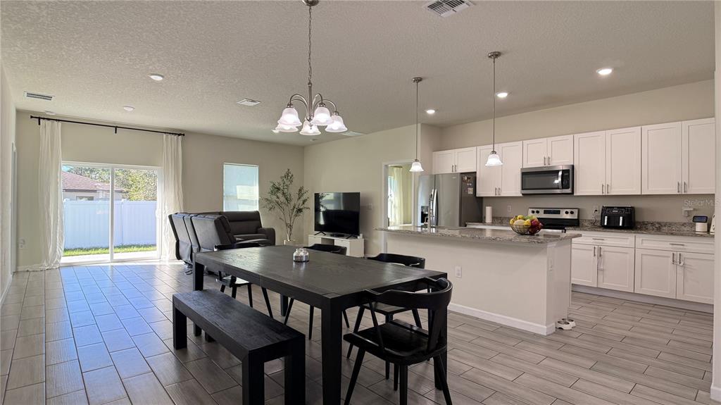 An open-concept kitchen and dining area features white cabinetry, a kitchen island, and tile flooring — 2129 HIBISCUS PLACE, POINCIANA, FL