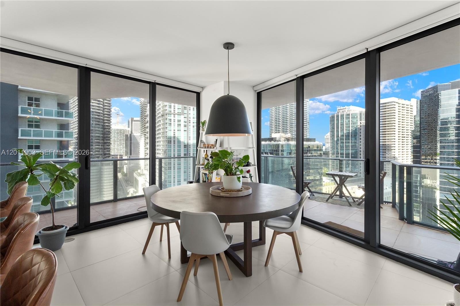 A dining area features a round wooden table, modern chairs, and floor-to-ceiling windows with city views — 1300 S Miami Ave # 2001, Miami FL 33130, MIAMI, FL