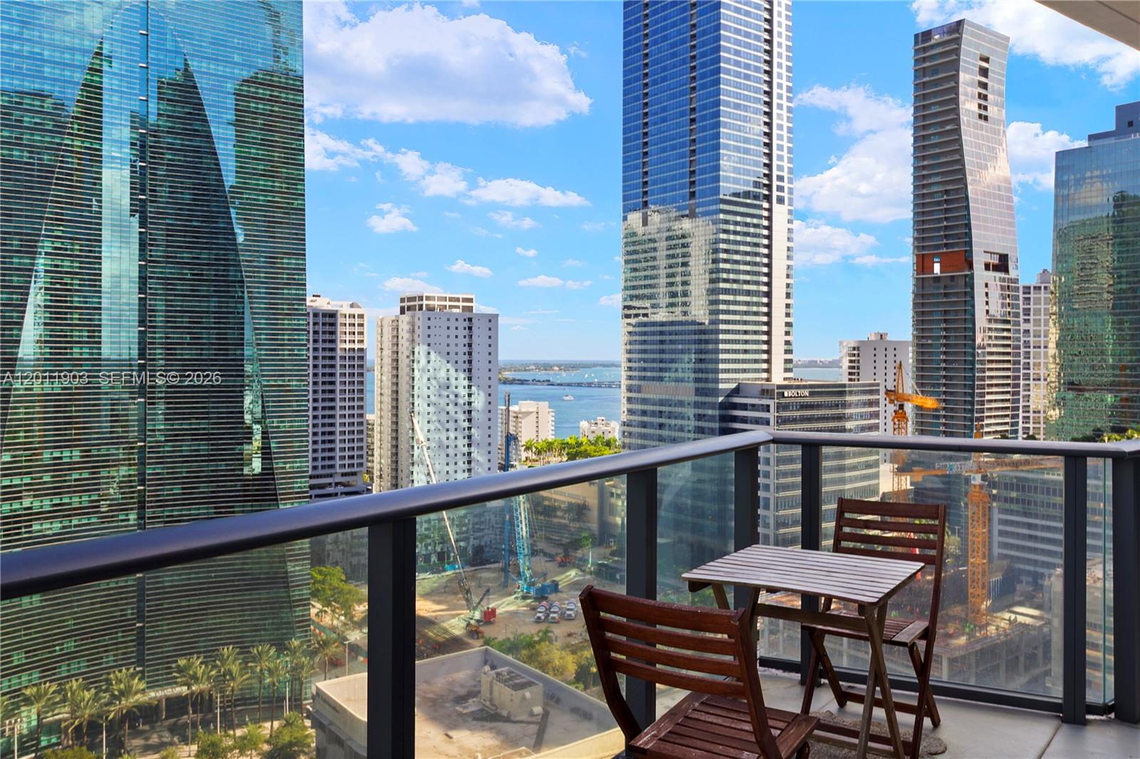 A balcony with a small wooden table and two chairs overlooks a dense city skyline — 1300 S Miami Ave # 2001, Miami FL 33130, MIAMI, FL