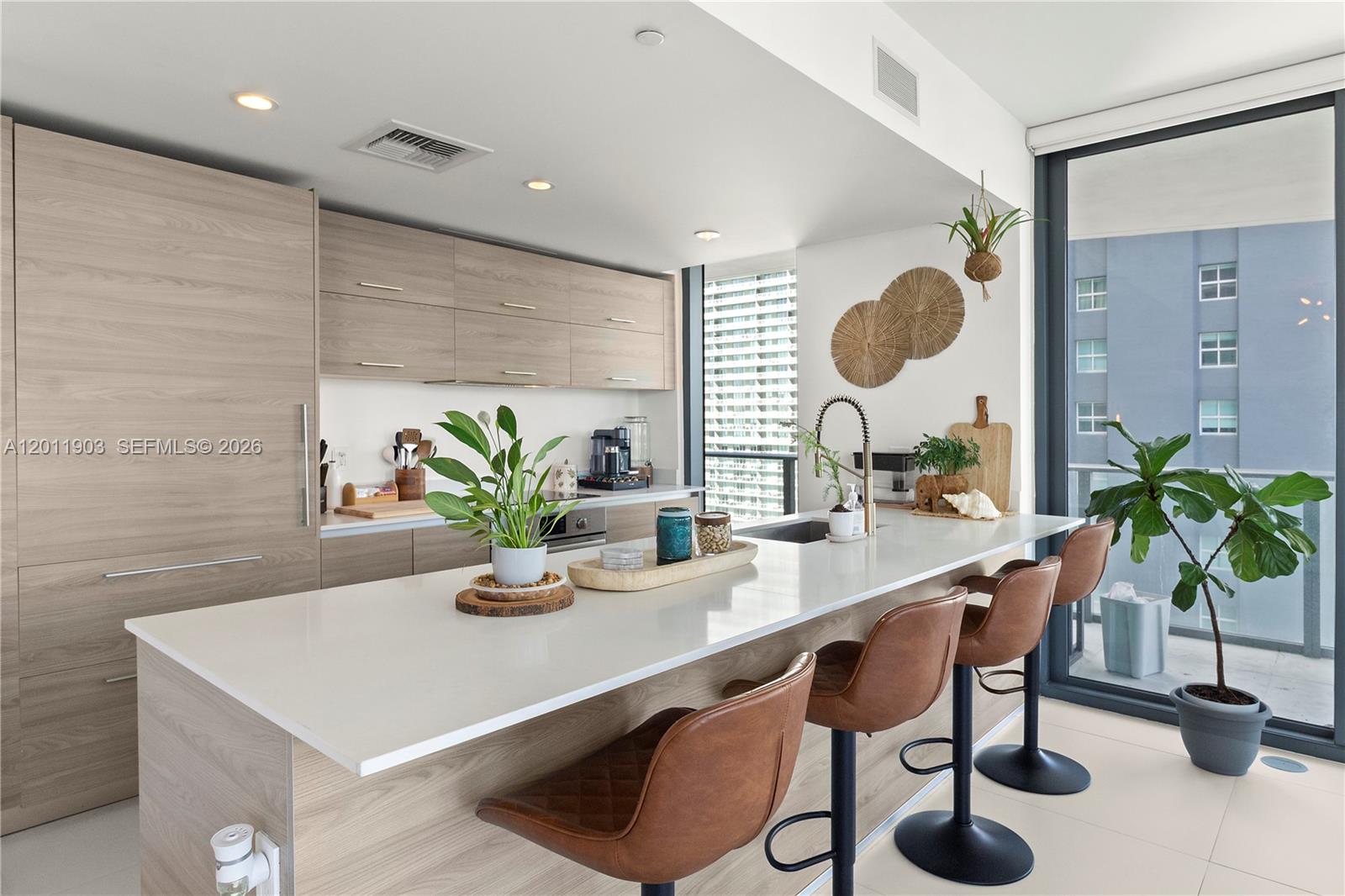 A modern kitchen features light wood cabinetry, a white quartz island, and three leather barstools — 1300 S Miami Ave # 2001, Miami FL 33130, MIAMI, FL