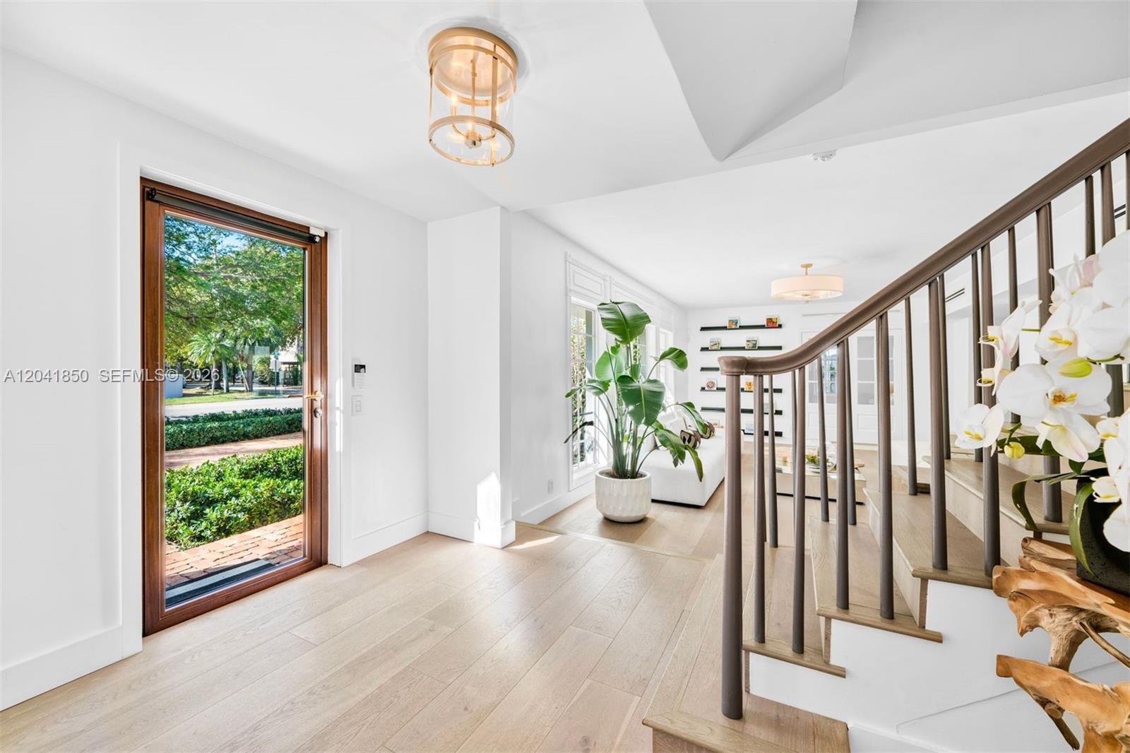 A bright entryway features light wood flooring, a staircase with dark railings, and a glass door — 939 W 47th Ct, Miami Beach FL 33140, MIAMI BEACH, FL