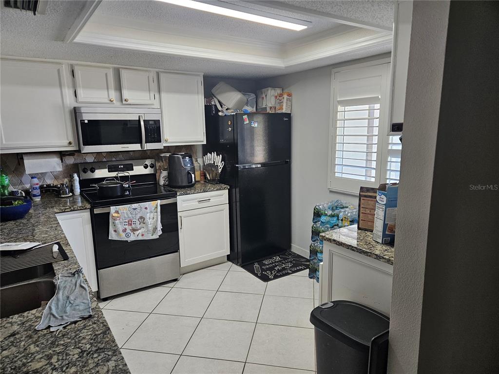 A kitchen features white cabinets, granite countertops, a black refrigerator, and a black stove — 2900 GROVEWOOD BOULEVARD E UNIT C, PALM HARBOR, FL