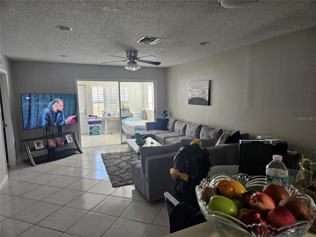 A living room features a gray sectional sofa, a television, and a glass-enclosed patio area — 2900 GROVEWOOD BOULEVARD E UNIT C, PALM HARBOR, FL