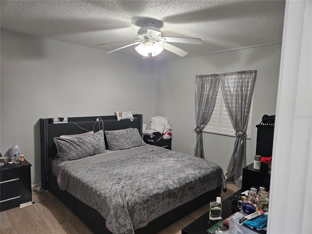 A bedroom features a gray upholstered bed, matching nightstands, a ceiling fan, and silver curtains — 2900 GROVEWOOD BOULEVARD E UNIT C, PALM HARBOR, FL