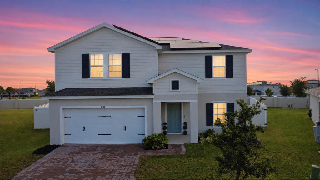 A two-story house with a white garage, light siding, and solar panels at sunset — 1141 LEXINGTON LANE, HAINES CITY, FL