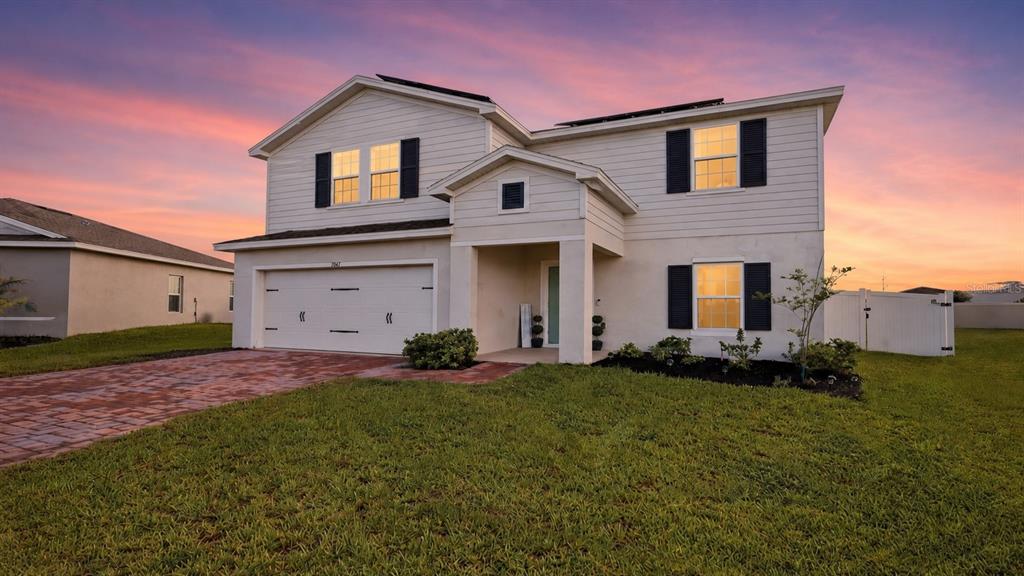 A two-story house with light siding, a two-car garage, and a paved driveway at sunset — 1141 LEXINGTON LANE, HAINES CITY, FL