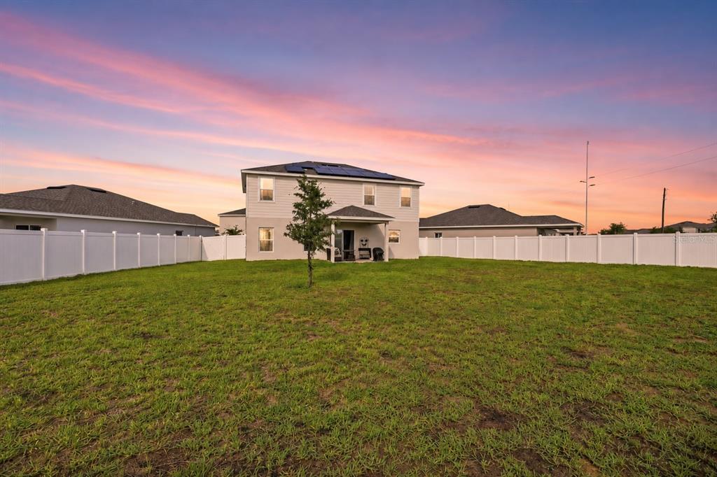 The rear exterior of a two-story house with a fenced yard at sunset — 1141 LEXINGTON LANE, HAINES CITY, FL