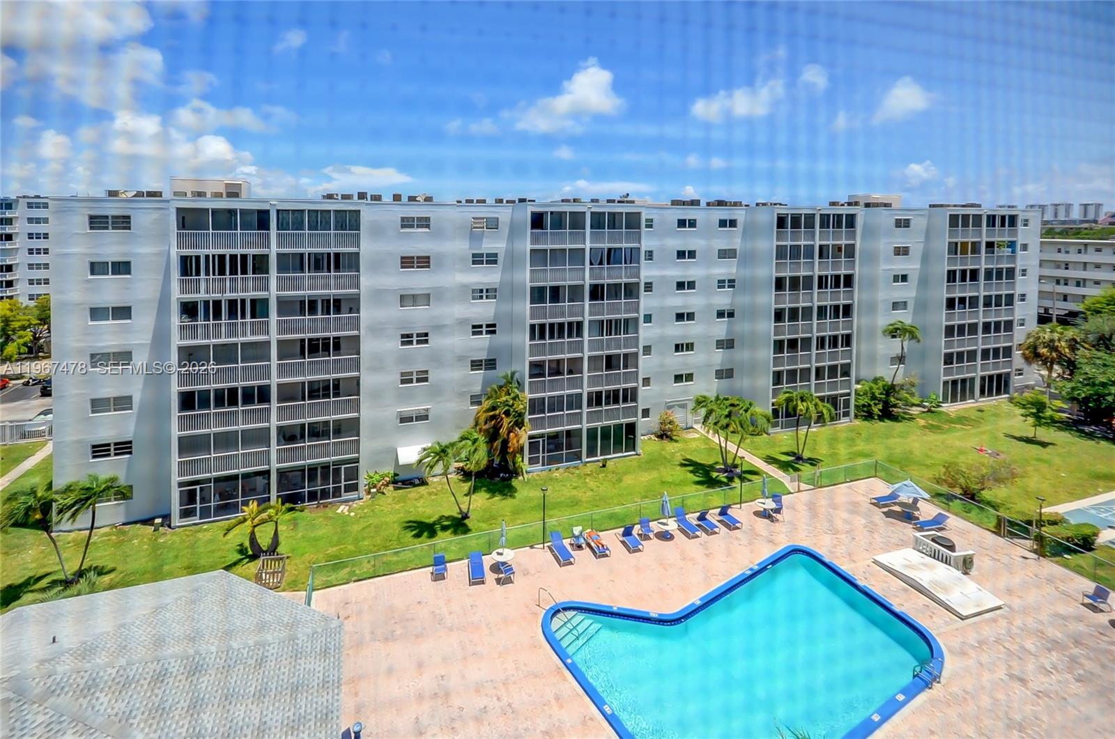 An exterior view of a multi-story apartment building with a swimming pool in the foreground — 301 NE 14th Ave # 702, Hallandale Beach FL 33009, HALLANDALE BEACH, FL