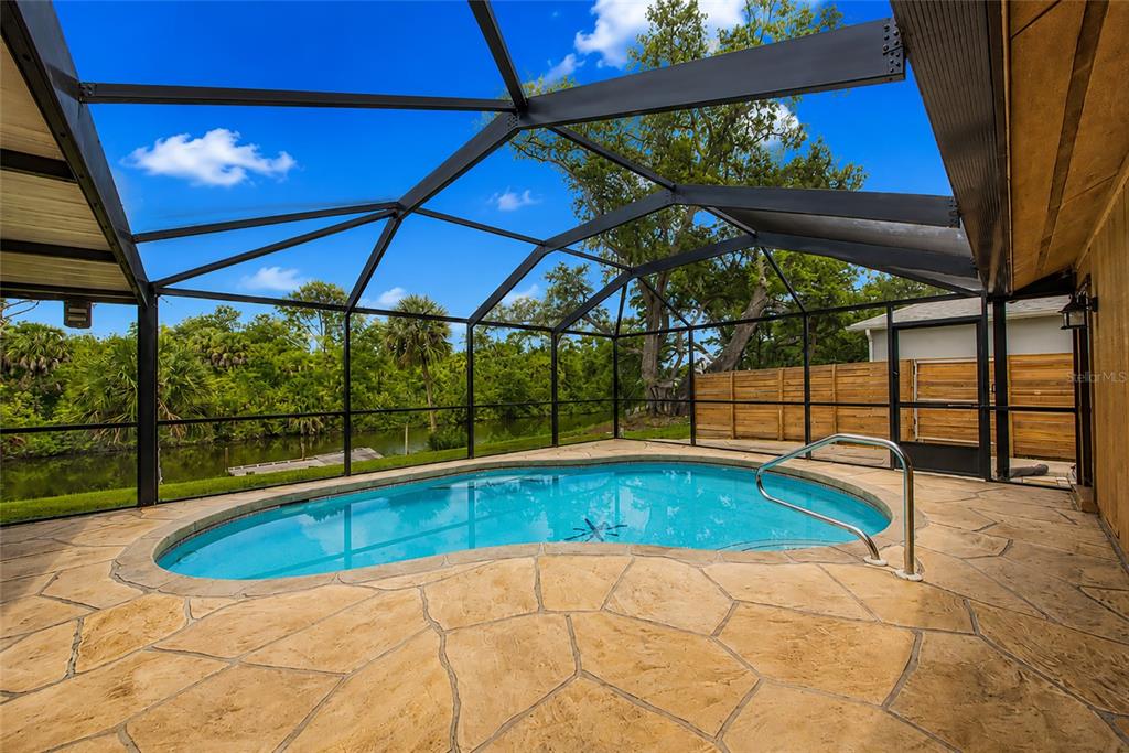 A screened-in pool patio features a kidney-shaped pool, stone-patterned deck, and views of a canal — 225 HOFFER STREET, PORT CHARLOTTE, FL
