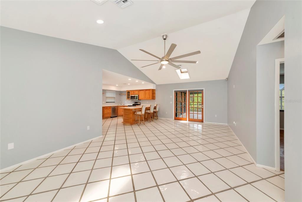 A spacious room with vaulted ceilings, tile flooring, and an open kitchen with wooden cabinets — 225 HOFFER STREET, PORT CHARLOTTE, FL