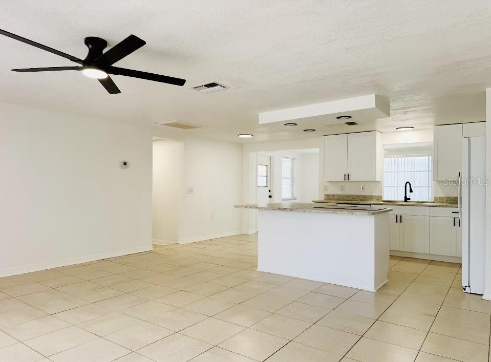 A bright kitchen features white cabinets, granite countertops, a central island, and tiled flooring — 7412 UNIVERSITY DRIVE, HUDSON, FL