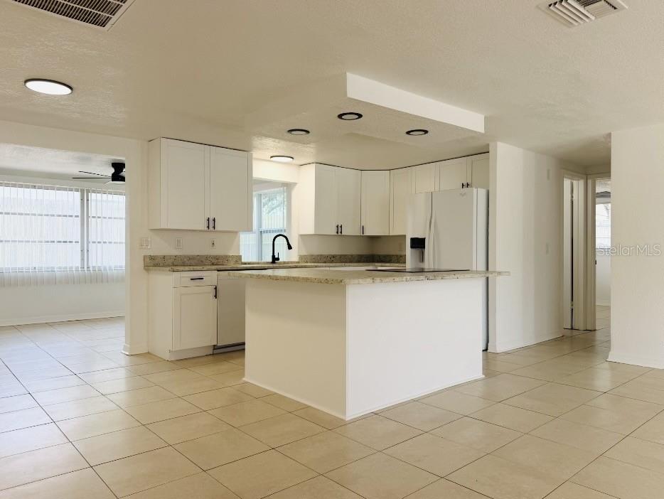 A kitchen features white cabinets, granite countertops, a central island, and light-colored tile flooring — 7412 UNIVERSITY DRIVE, HUDSON, FL